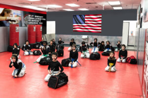Kids sitting on the floor during training with the Wall with American flag at Tiger Schulmann's
