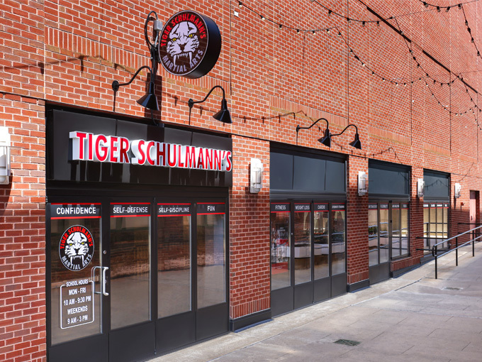 A brick building with a black awning reads "TIGER SCHULMANN'S" in red and white. Glass doors & windows show martial arts logos.