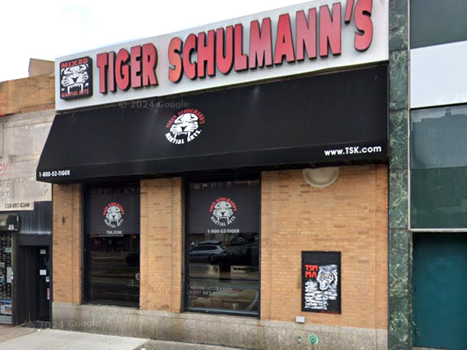 A brick storefront displaying "TIGER SCHULMANN'S" in red and white letters with martial arts logos and website information.