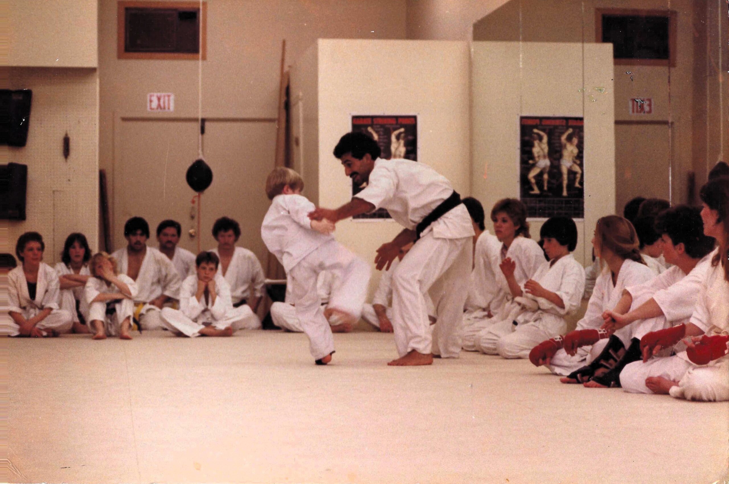 A man with dark hair and mustache sparring with a small boy.