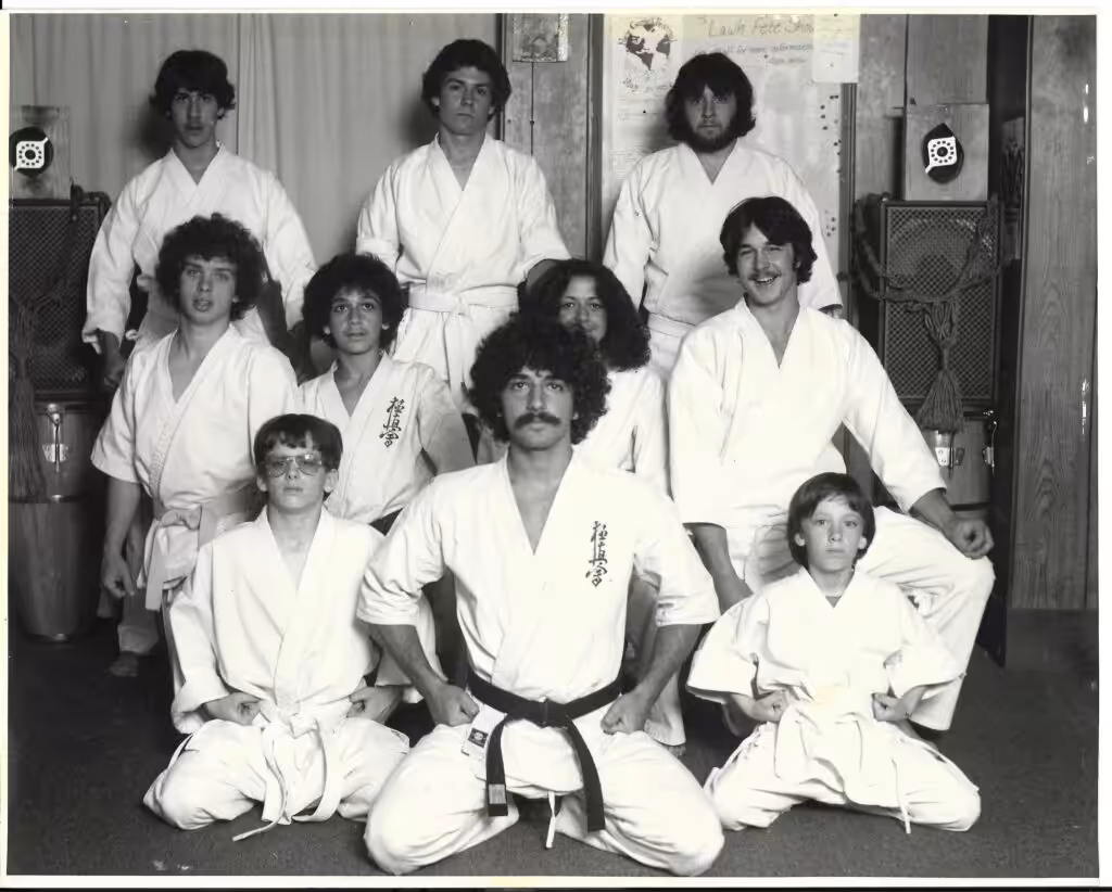 A black and white portrait of five men and three boys in gis, with one man in the center having a black belt.