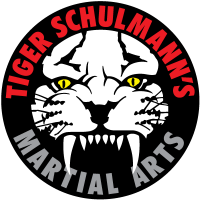 Circular logo with a white tiger head, yellow eyes, and black and red "TIGER SCHULMANN'S MARTIAL ARTS" text.